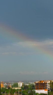 Dikey video. Şehir üzerindeki yağmurdan sonra gökkuşağının hızlanması, görünür ve kaybolur..