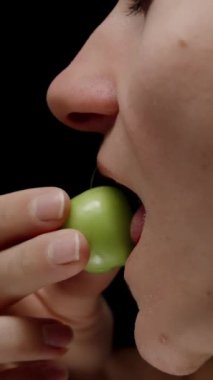 Dikey video. Genç Kadın Yeşil Olgunlaşmamış Vişne Eriği ve Kaynak 'tan Grimaces ısırıyor. Yavaş Hareket.