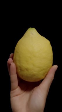 Dikey video. Kara Arkaplanda Alttan Bir Büyük Limon Bir Kadının Elinde Görünüyor.