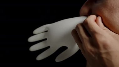 Sakallı bir adam siyah arka planda beyaz tıbbi eldiveni ağzıyla şişirir. Yavaş Hareket.