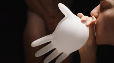 Genç bir kadın, arka planda kendisini saran çıplak bir adamla lateks tıp eldivenini şişiriyor. Tıbbi İnceleme Konsepti.