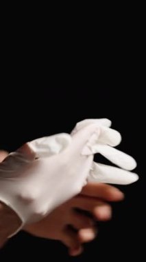 Dikey video. Erkek ve Kadın Tıbbi Eldiven Giyiyor, Beyaz ve Siyah, Muayene ya da Ameliyata Hazırlanıyor. Siyah Arkaplan.