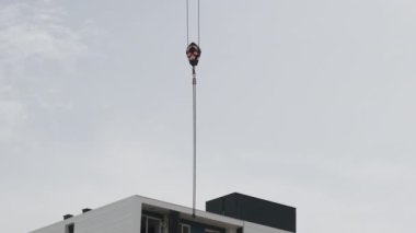 İnşaat alanındaki yüksek katlı bir vinçten zincire bağlı bir vinç bir binanın çatısına karşı gökyüzünde yükseliyor..