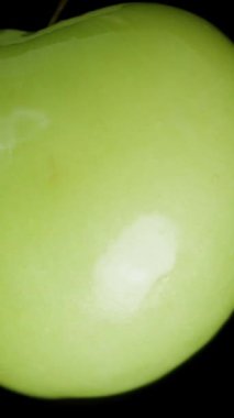 Dikey video. Düşme kavramı, bir Yeşil Erik Siyah Arkaplanda Dönerken Daha da Uzaklaşır. Makro Kaydırıcı.