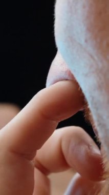 Dikey video. Sakallı Adam, akıllı telefonuyla haber akışına kayarken burnunu karıştırıyor ya da sadece fotoğraflara bakıyor..