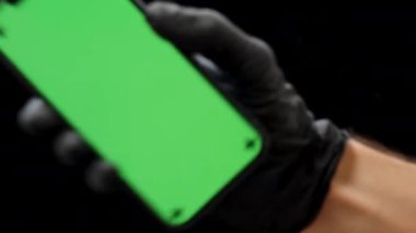 Siyah Eldiven İçinde Bir El Yeşil Ekran Kromatonlu Akıllı Telefonu Tutuyor, Siyah Arkaplanda, Yatay Oryantasyon Ekrandan Uzaklaşıyor.