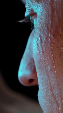 Dikey video. Bir erkeğin yüzünden ter damlıyor, Smartphone 'undaki sosyal medyada etkin bir şekilde kaydırmaya devam ederken onu siliyor. Telefon Bağımlılığı Konsepti.