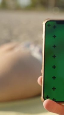 Arkaplanda Güneş Banyosu yapan bir kadınla Yeşil Ekran Modeli ve Erkek Elindeki İz İşaretli Akıllı Telefon.