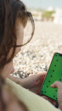 Plajda güneşlenen ve Smartphone 'da Yeşil Ekran Modeli ve İzleme İşaretleri olan bir şeye bakan kadın..