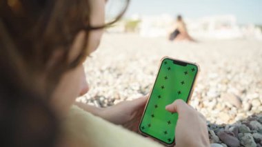 Plajda uzanan ve Smartphone 'u boş yeşil ekran modeliyle çalan kadın..