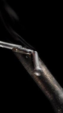 Dikey video. Lehim Demiri Ucundaki Teneke Tel Kablo, Siyah Arkaplan 'a Yakın Çekim. Metal Boncuk.