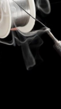 Dikey video. Isıtmalı uçta eriyen demir lehim için teneke merhem. Siyah Arkaplanda Zehirli Duman.