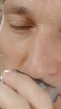 Dikey video. Sakallı Adam, aynanın önünde elektrikli jiletle bıyığını tıraş ediyor. Yakın plan. Yavaş Hareket.