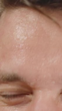 Dikey video. Genç adam aynada kendine bakıyor ve yüzünü suyla yıkıyor, yavaş hareket ediyor..