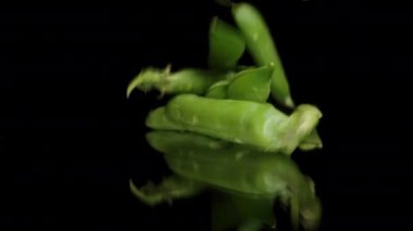 Yeşil Bezelye Kabukları yavaşça yukarıdan siyah aynalı bir masaya düşüyorlar ve kameraya doğru dönüyorlar..