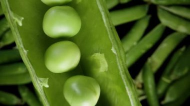 Üst manzara, içinde bezelyeler olan yavaş düşen bezelye kabuğu, yeşil kabuklar ve siyah arka plan yığını. Makro Doli.