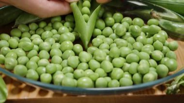 Taze bir bezelye kabuğunu açmak ve bezelyeler diğer fasulyelerle birlikte tabağa düşmek. Yavaş çekim.