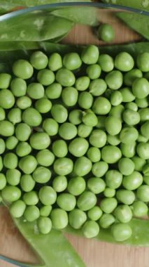 Dikey video. Üst manzara, temiz yeşil bezelyeleri kameraya yaklaştırmak ve tabağı sallamak, yavaş çekim.