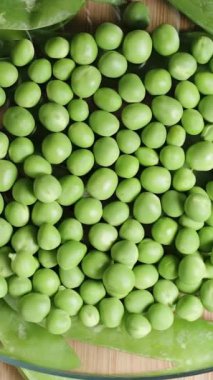 Dikey video. Tahta bir masada taze bezelye kabuklarını temizledim ve bir plaka doli zoom 'da, üst manzara.