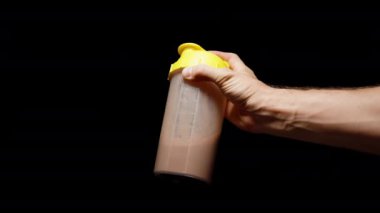 Siyah Arkaplan 'da izole edilmiş bir erkek el, protein içeceğiyle bir Shaker' ı sallıyor ve onu yaklaştırıyor..