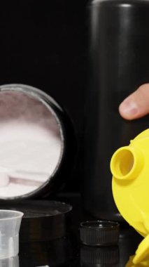 Dikey video. Siyah Masa 'ya konan Spor İlaveleri, Bir Ölçüm Kupasına Kırmızı Sıvı Döken Adam. Güç Eğitimi ve Doping.