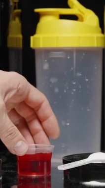 Dikey video. Eğitimden önce atletler için küçük bir fincan kırmızı likit içilebilir takviyesi bir adam ve bir Shaker tarafından masadan alınır..