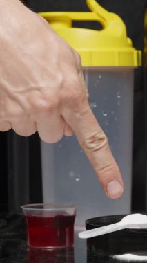 Dikey video. Bir adam parmağıyla işaret eder ve masanın üzerinde farklı pudralanmış ve sıvılaşmış ürünler gösterir. Spor Beslenme Seçimi.