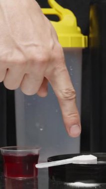 Dikey video. Spor malzemelerinin çeşitliliği, bir adam alınmaması gerekenleri işaret eder ve bir kaşık protein tozu alır..