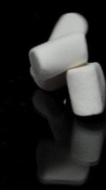 Dikey video. Beyaz Marshmallow Yığını Siyah Yansıtıcı Masa 'ya Düşüyor, Yavaş Hareket. Şeker ve Şeker Zararı kavramı.