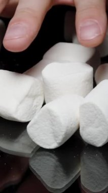 Dikey video. Siyah Masa ve Şeker Bağımlılığı 'ndan Marşmelov Yığını Alan Bir Erkek El' in Yakın Çekimi.