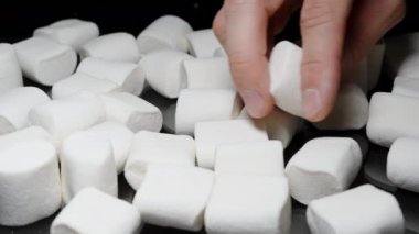 Beyaz Marshmallow 'u İnceleyen Erkek El, Siyah Bir Arkaplan Karşısında Masaya Bir Çok Şekerleme Dağıldı.