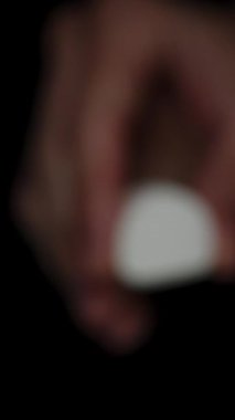 Dikey video. Marshmallow in Male Hand yavaşça karanlıktan yaklaşıyor, onu sıkıyor ve yumuşak dokusunu gösteriyor..