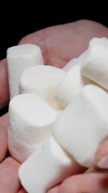 Dikey video. Adam yavaşça ellerinden bir sürü beyaz lokum döküyor. Sağlıksız Tatlı Yemek kavramı.