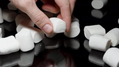 Siyah Yansıtıcı Masa 'ya serpilmiş beyaz şekerlemeler, Bir El Alma ve Sıkan Yumuşak Dokudan Zevk Alma.