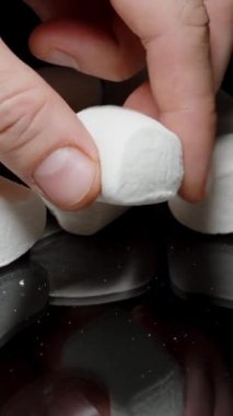 Dikey video. Siyah Yansıtıcı Masa 'ya serpilmiş beyaz şekerlemeler, Bir El Alma ve Sıkan Yumuşak Dokudan Zevk Alma.