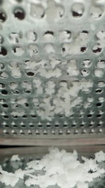 Dikey video. Grating Coconut Pulp on a Fine Metal Grater, Low Angle Macro View, Slow Motion. Siyah Ayna Tablosu.