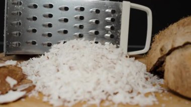 Rendelenmiş hindistan cevizi hamuru yığını, arka planda metal rendesi, çatlak kabuğa odaklanma kaymaları.