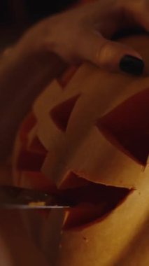 Dikey video. Siyah tırnaklı bir kadın Cadılar Bayramı için Cadılar Bayramı Feneri oyuyor. Mum ışığında, rahat bir evde..