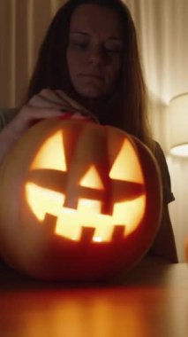 Dikey video. Cadılar Bayramı 'nı Bekleyen Ev Gecesi, Kadın Fener' in İçini Gözler. Karanlık Bir Odada Masadaki Balkabakları ve Mumlar.