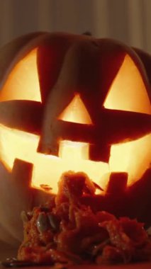 Dikey video. Cadılar Bayramı arka planı. Mum ışığından Jack-o '-Lantern ve Balkabağı Masada. Balkabağı ezmesi ve tohumlar ağızdan döküldü..