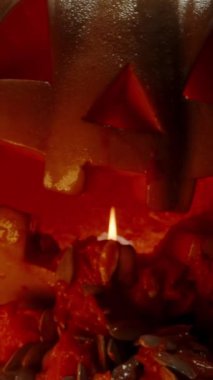 Dikey video. Terli Jack-O '-Lantern, Ağızdan dökülen tohumlar ve hamur şeklindeki bağırsaklar, İçerideki Kamera Hareketleri, Yakıcı Mum' u yakın çekim.