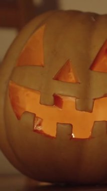 Dikey video. Bir Jack-O-Lantern 'in yakın çekimi Duvara Gölge Düşüren Bir Gölge, İçeride yanan bir mum, Cadılar Bayramı' nda karanlık bir oda.