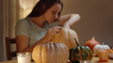 Lambaların Ilık Işığındaki Uzun Saçlı Esmer Cadılar Bayramı 'nda Balkabağı İçini Temizliyor. Masada çeşitli Mini Pumpkins 'ler var. Tatil Dekorasyonları.
