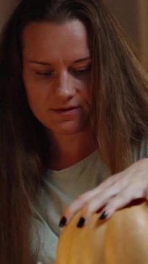 Dikey video. Cadılar Bayramı Dekorasyonları İçin Balkabağından Bıçak Çıkarmak İçin Çabalayan Genç Bir Kadın.