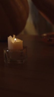 Dikey video. Mum Işığının Sıcak Tonları 'nda bir kadın balkabağından bir korkuluk oyuyor. Cadılar Bayramı Korku Konsepti.