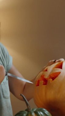 Dikey video. Mum ışığının ılık bir akşamında bir kadın Cadılar Bayramı 'nın sembolü olan balkabağından fener yapar..