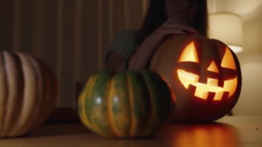 Karanlık bir odada, bir kadın Jack-O 'Lantern' in Lid 'ini açar ve içeri bakar, Yüzü mum ışığında ışıl ışıl parlar.