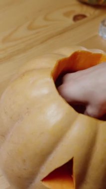 Dikey video. Masada Aile Gecesi, Cadılar Bayramına Hazırlık, Bir Kadın Balkabağının İçine Mum Koyuyor ve Işığı Yakıyor. Geleneksel bir Cadılar Bayramı Sembolü.
