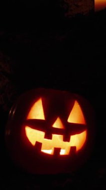 Dikey video. Bir mağarada beyaz bir hayalet, elinde bir balkabağı feneriyle duvarları aydınlatan Lid ve ışık akıntılarını kaldırıyor. Cadılar Bayramı Korku Konsepti.