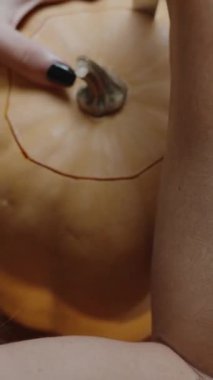 Dikey video. İçini çıkarmak için balkabağının üst kısmını oyan bir kadın. Cadılar Bayramı için bir Jack-o 'Lantern yaratıyorum. Arkadan Görünüm.